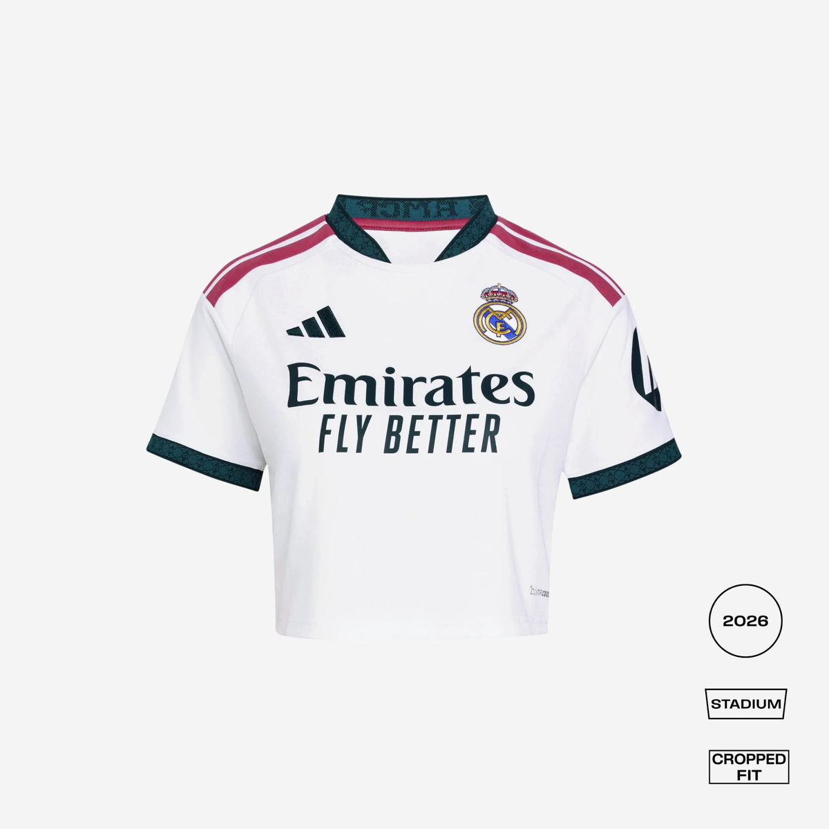 A white Real Madrid 2026 Stadium cropped fit jersey by adidas, featuring dark green and pink accents on the collar, shoulders, and cuffs, with the Emirates Fly Better sponsor logo on the front.
