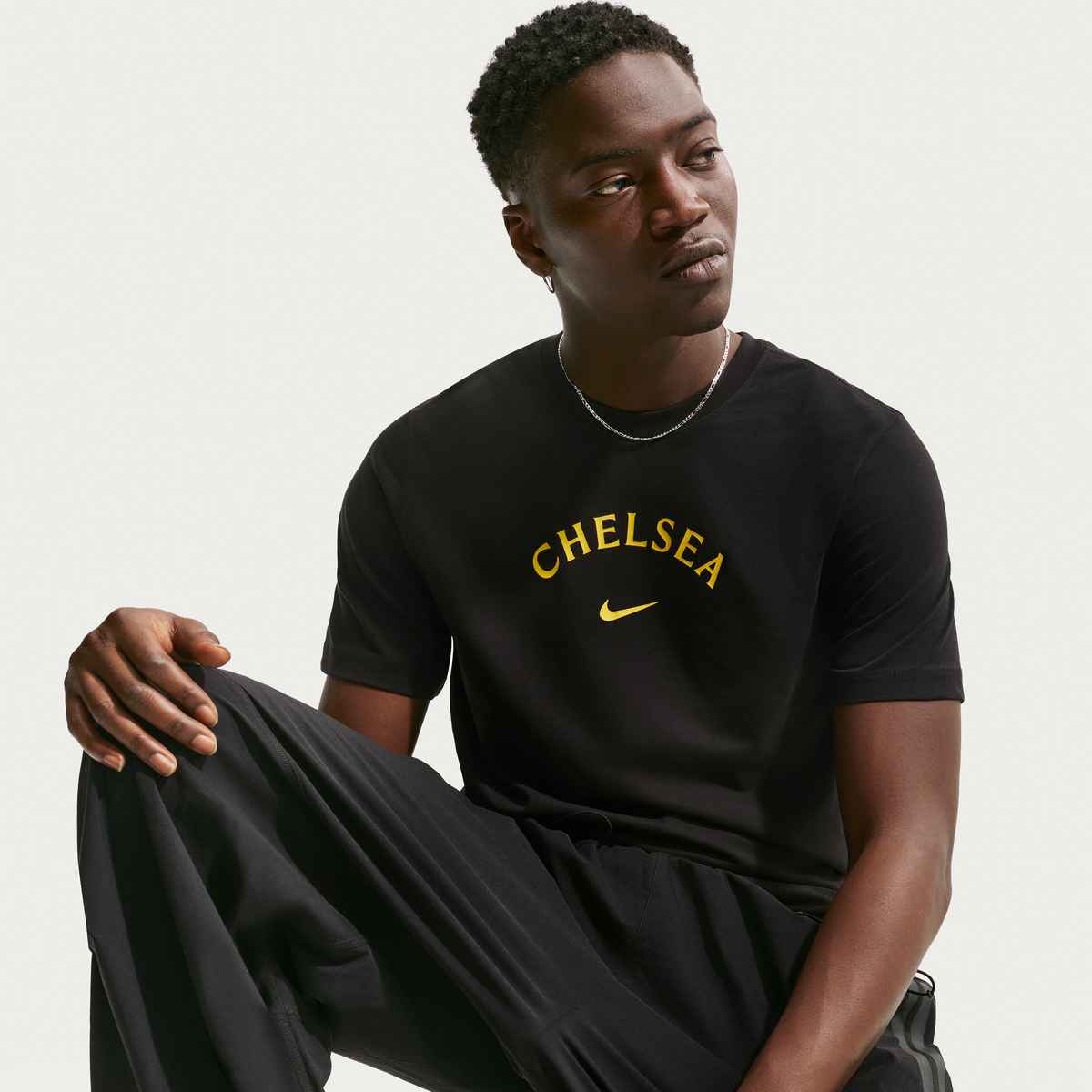 Person wearing a black 'Chelsea' t-shirt with a Nike logo on a light gray background