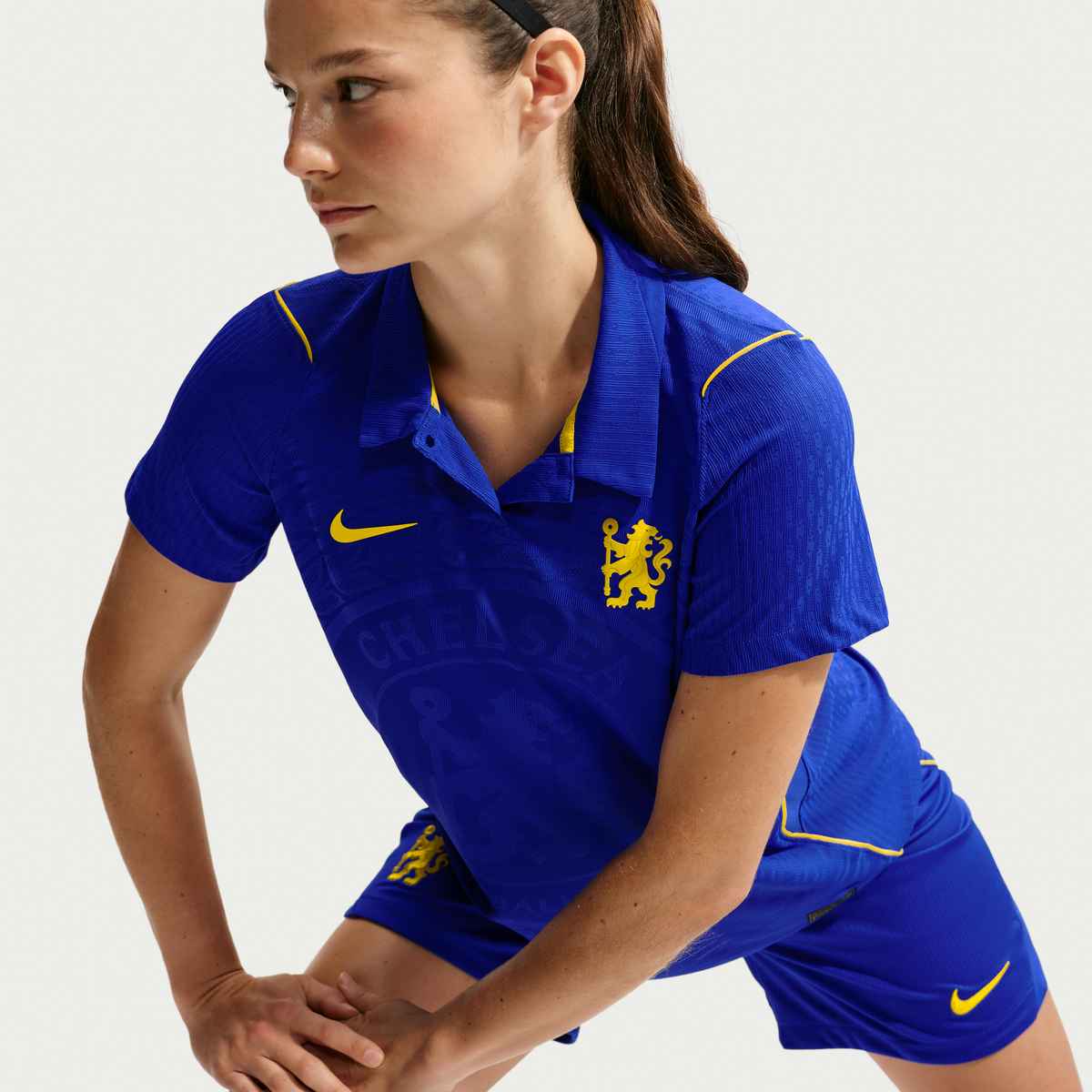Person wearing a blue sports outfit with yellow accents, featuring a logo on a light gray background