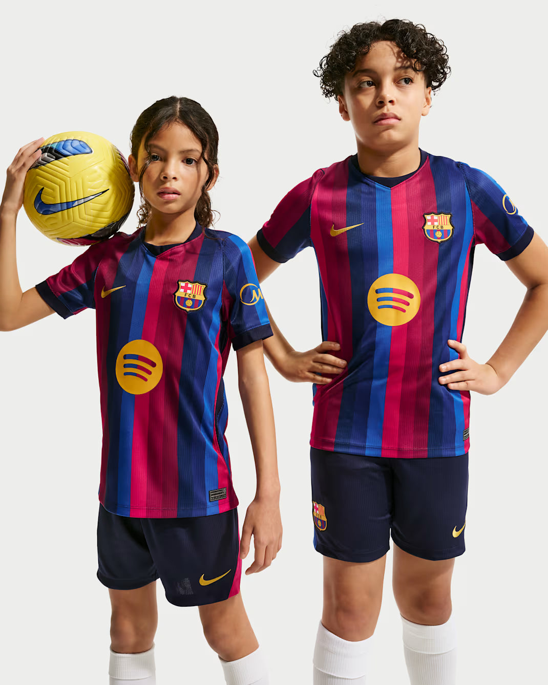 Two children wearing Barcelona soccer jerseys with a soccer ball on a white background