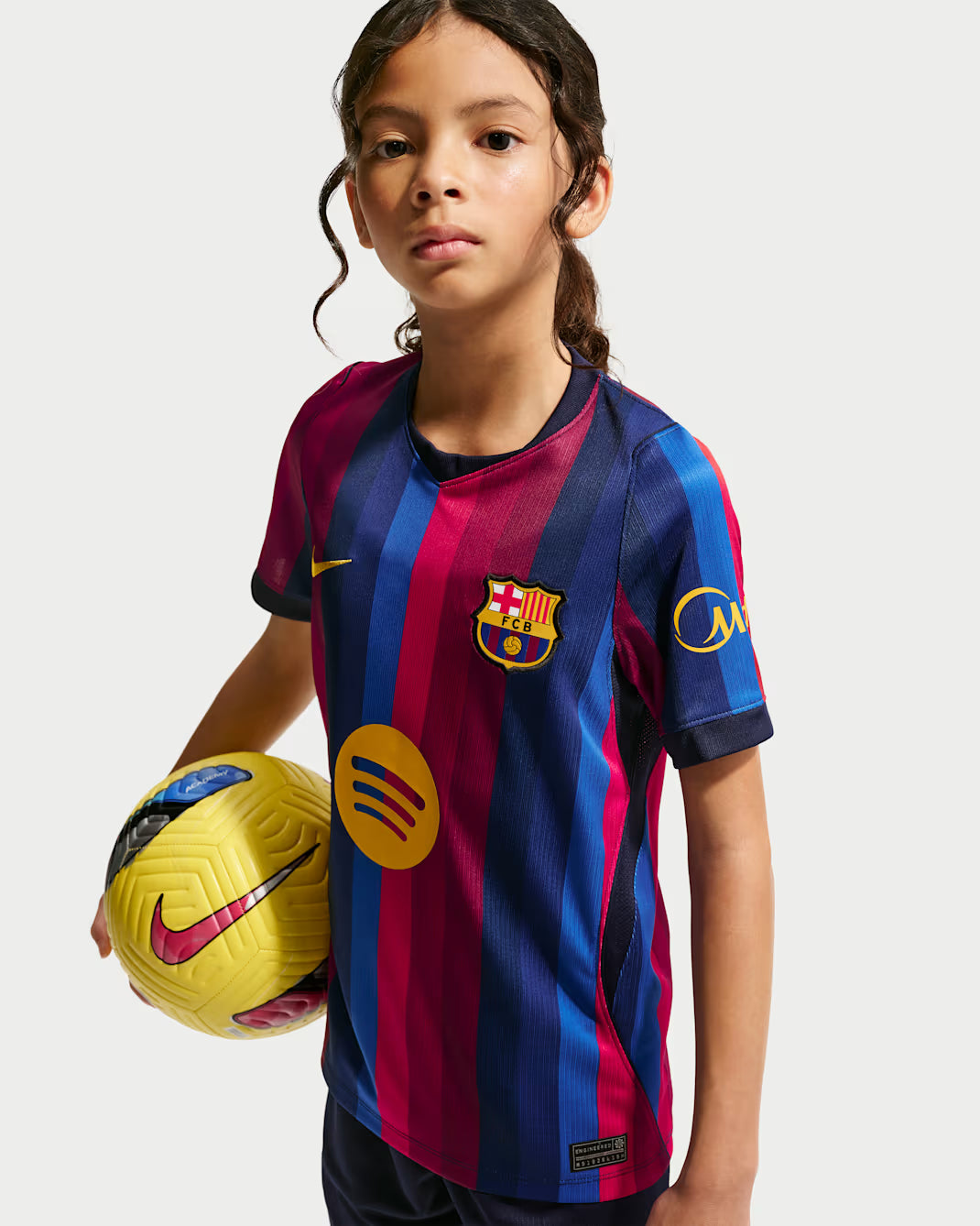 Child wearing a Barcelona soccer jersey holding a Nike soccer ball on a white background