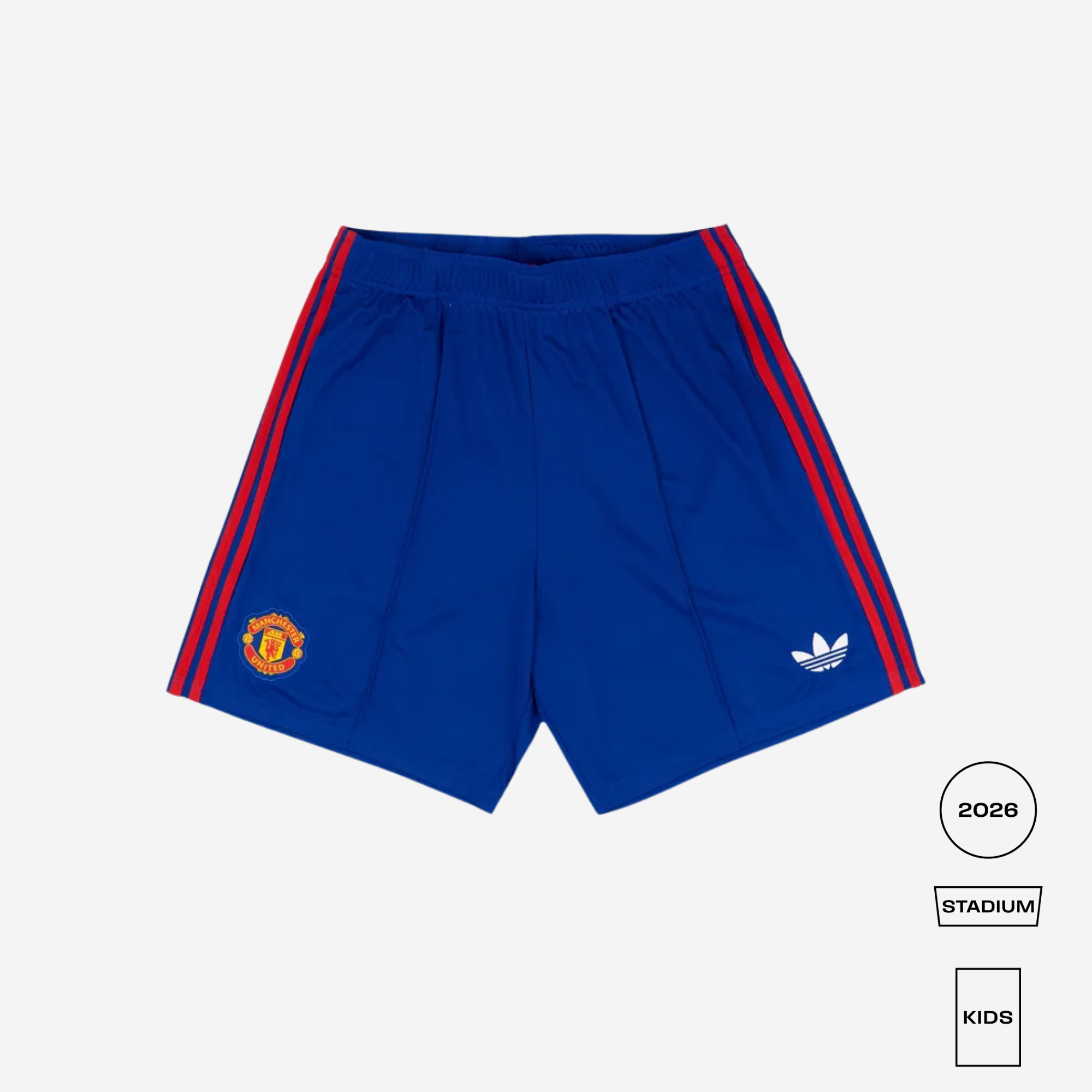 Blue Manchester United Adidas Stadium shorts for kids, featuring red side stripes, the Manchester United crest on the left leg, and the Adidas Trefoil logo on the right leg, shown on a light gray background with size/edition labels.