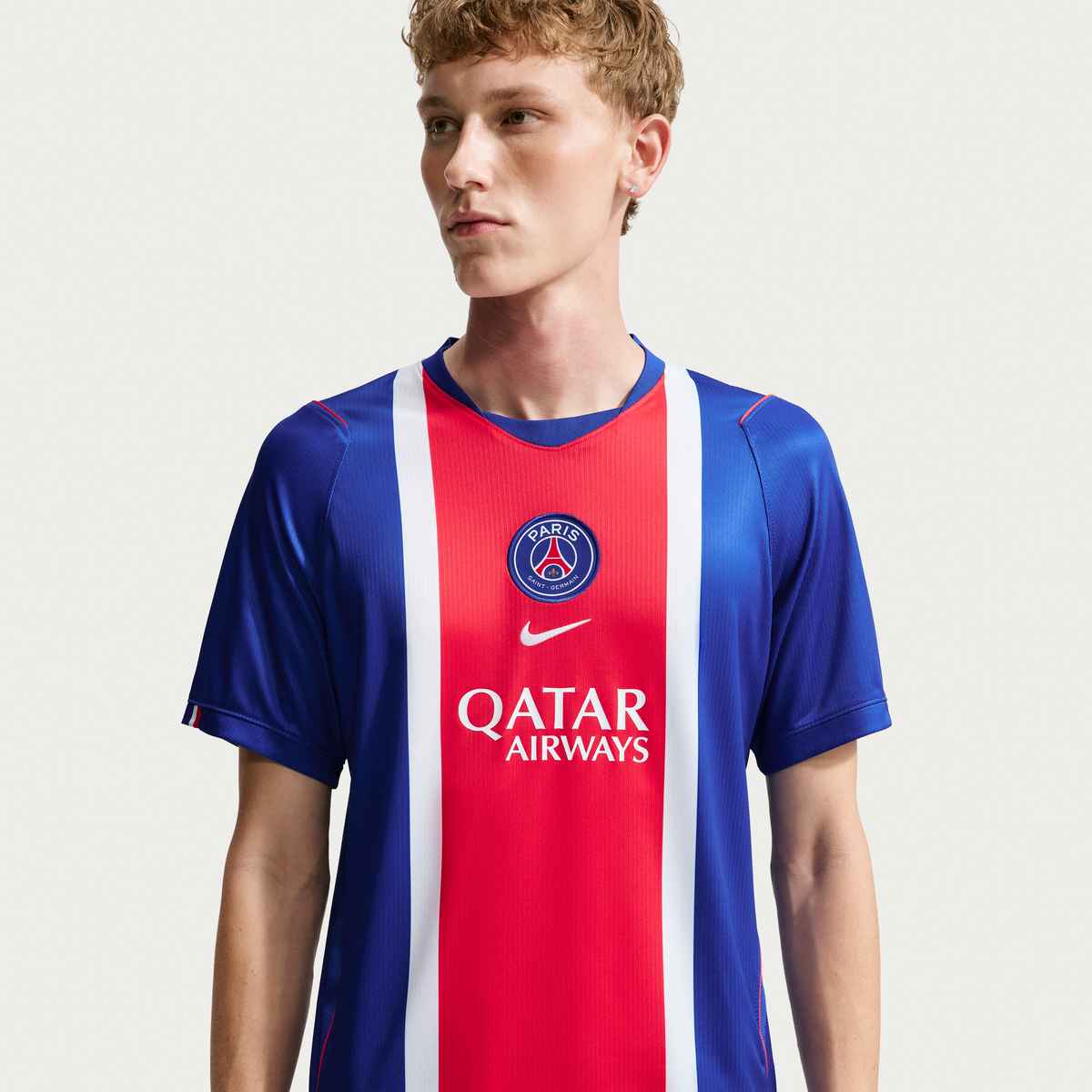 Person wearing a red, white, and blue sports jersey with Nike and Qatar Airways logos on a light gray background